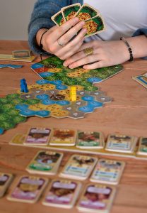 Spielsituation von El Dorado. Frau mit Karten in der Hand vor einer Kartenauslage